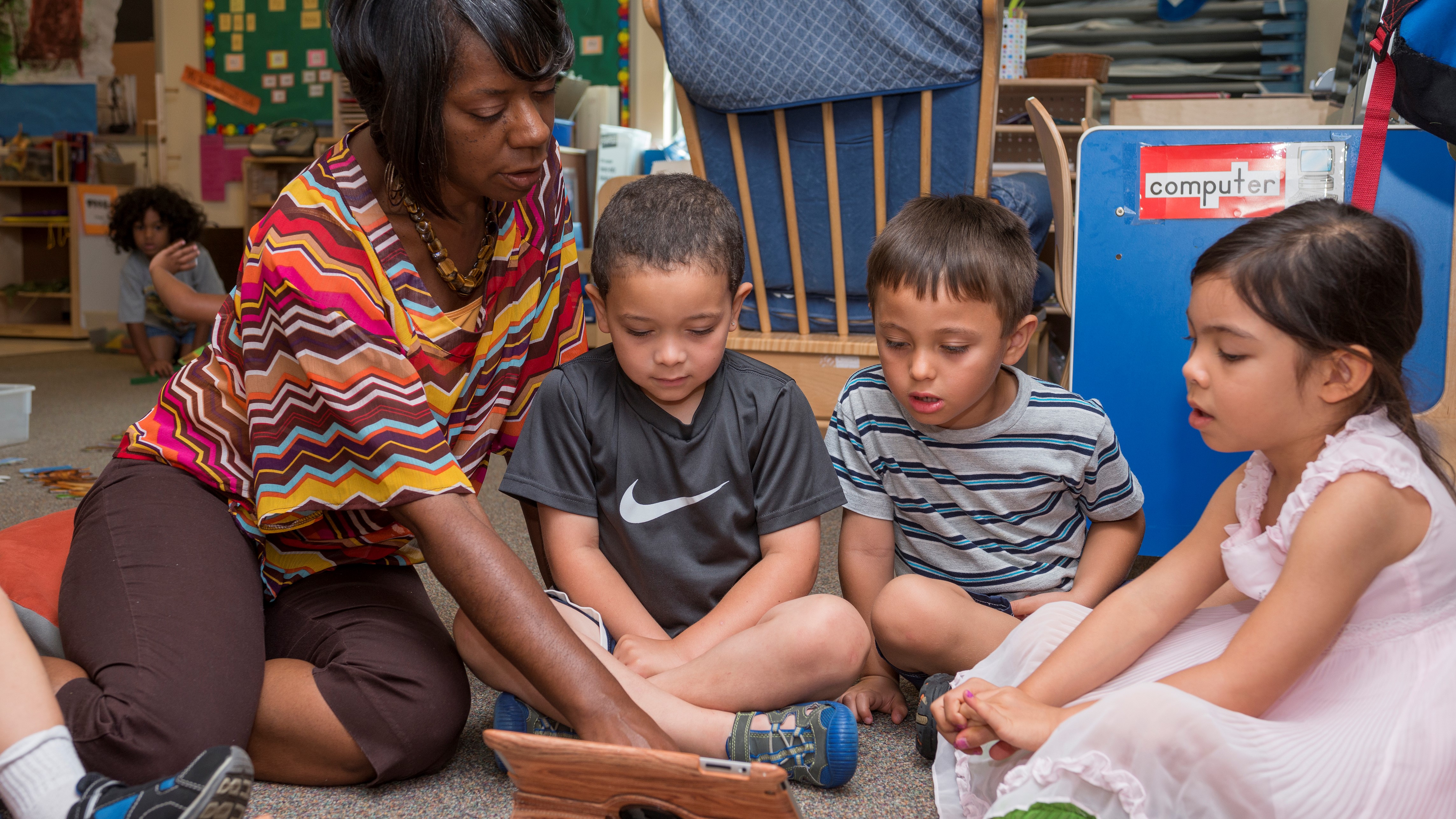 A teacher reads on an iPad with children.