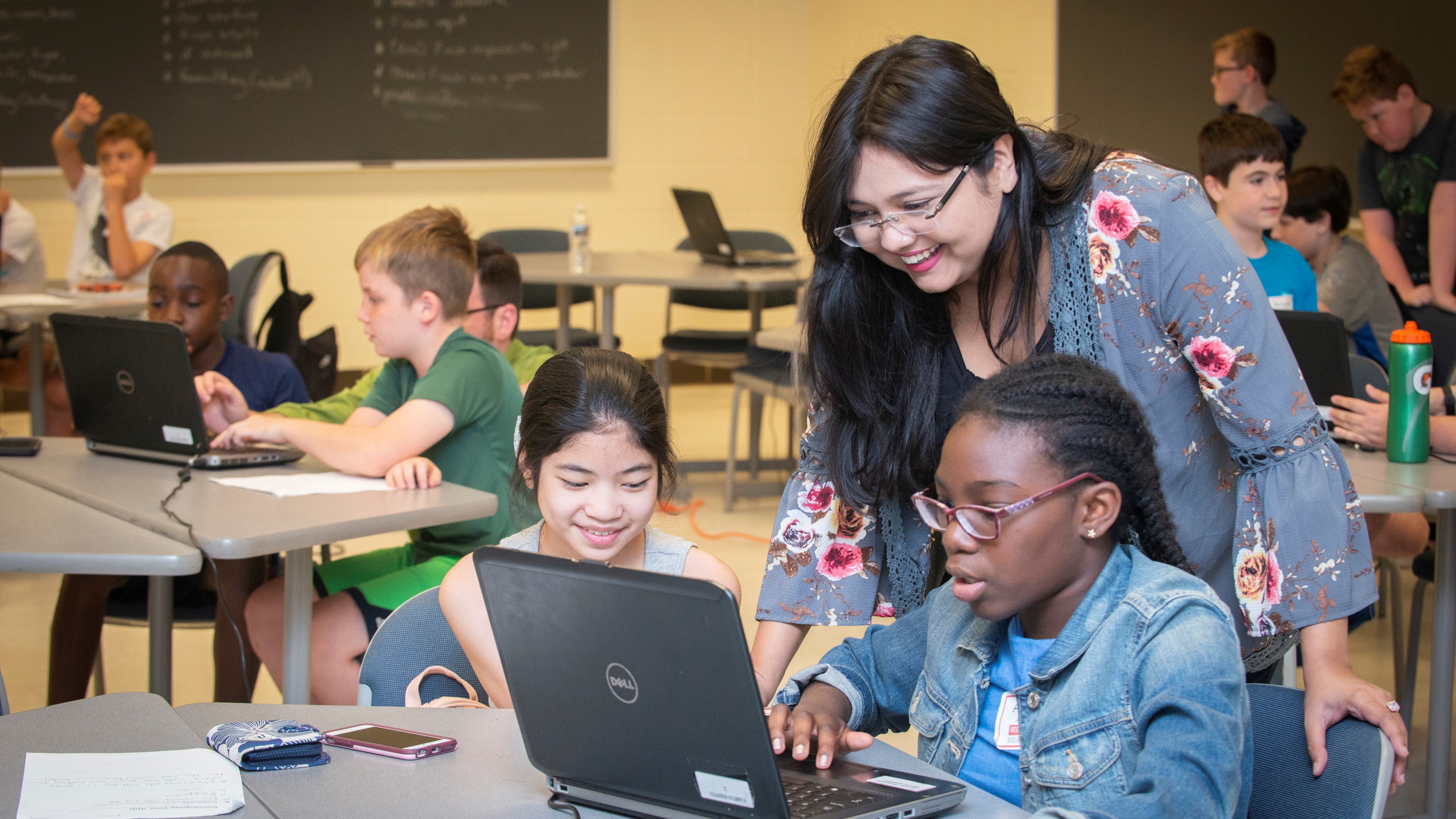 A University of Delaware student works on a computer science activity on a laptop with two middle school students.