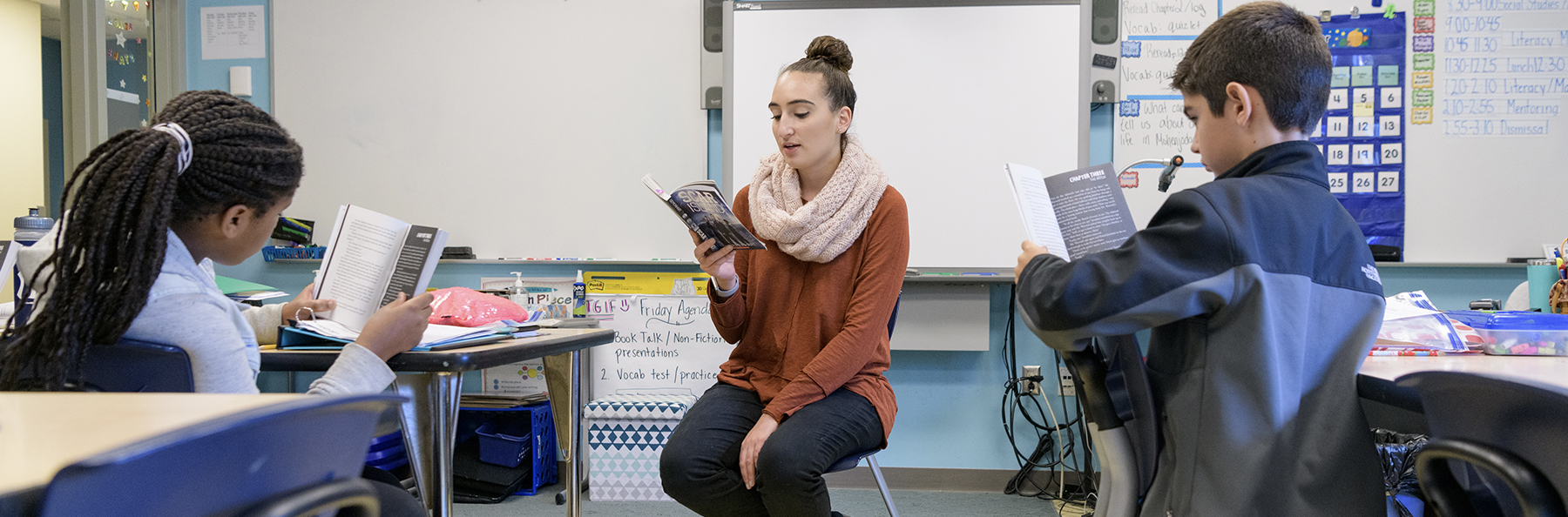 A student teacher reads to students in a classroom as they follow along in their books