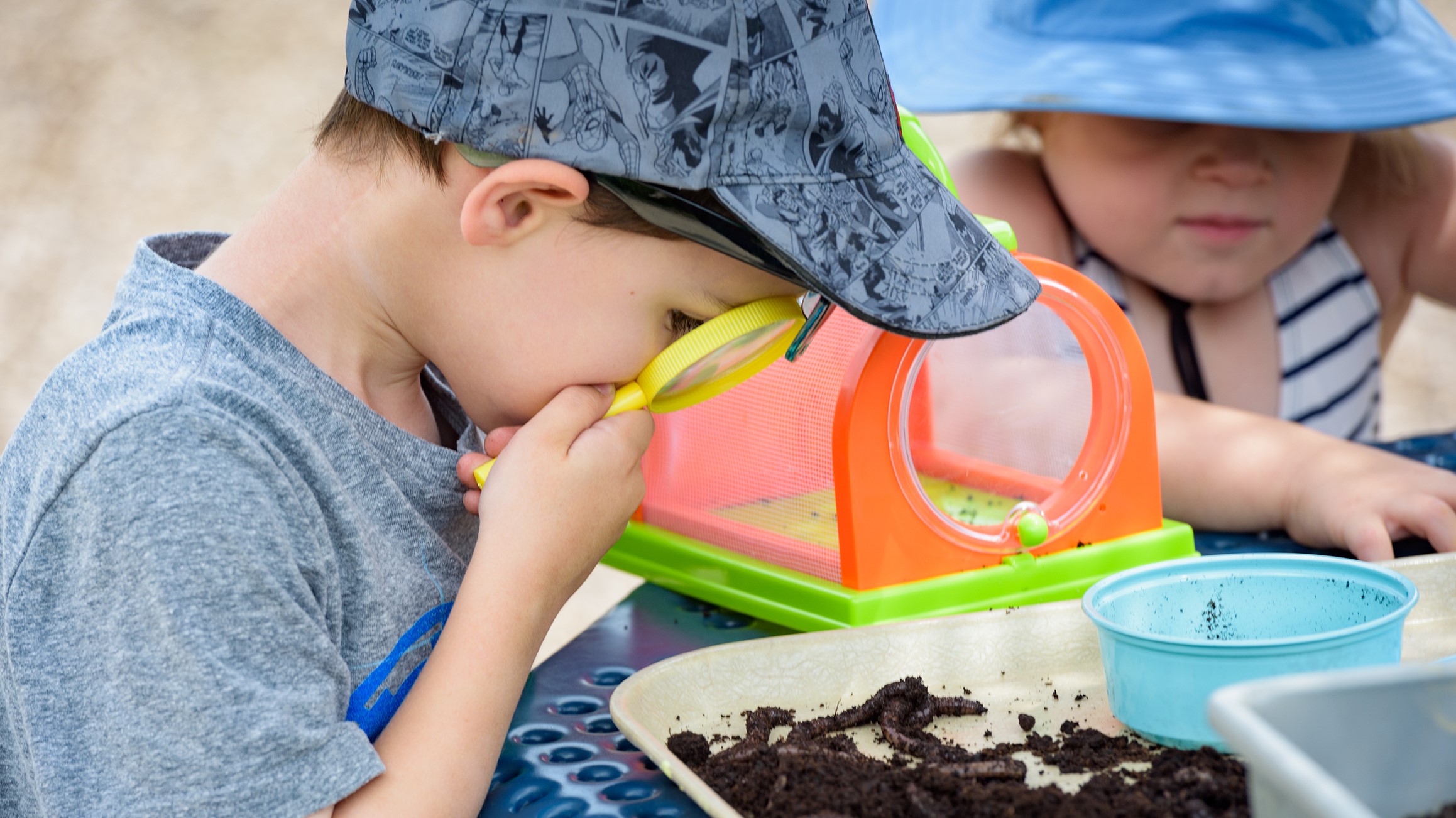 A boy studies earth worms with a magnifying glass during a nature-based activity.