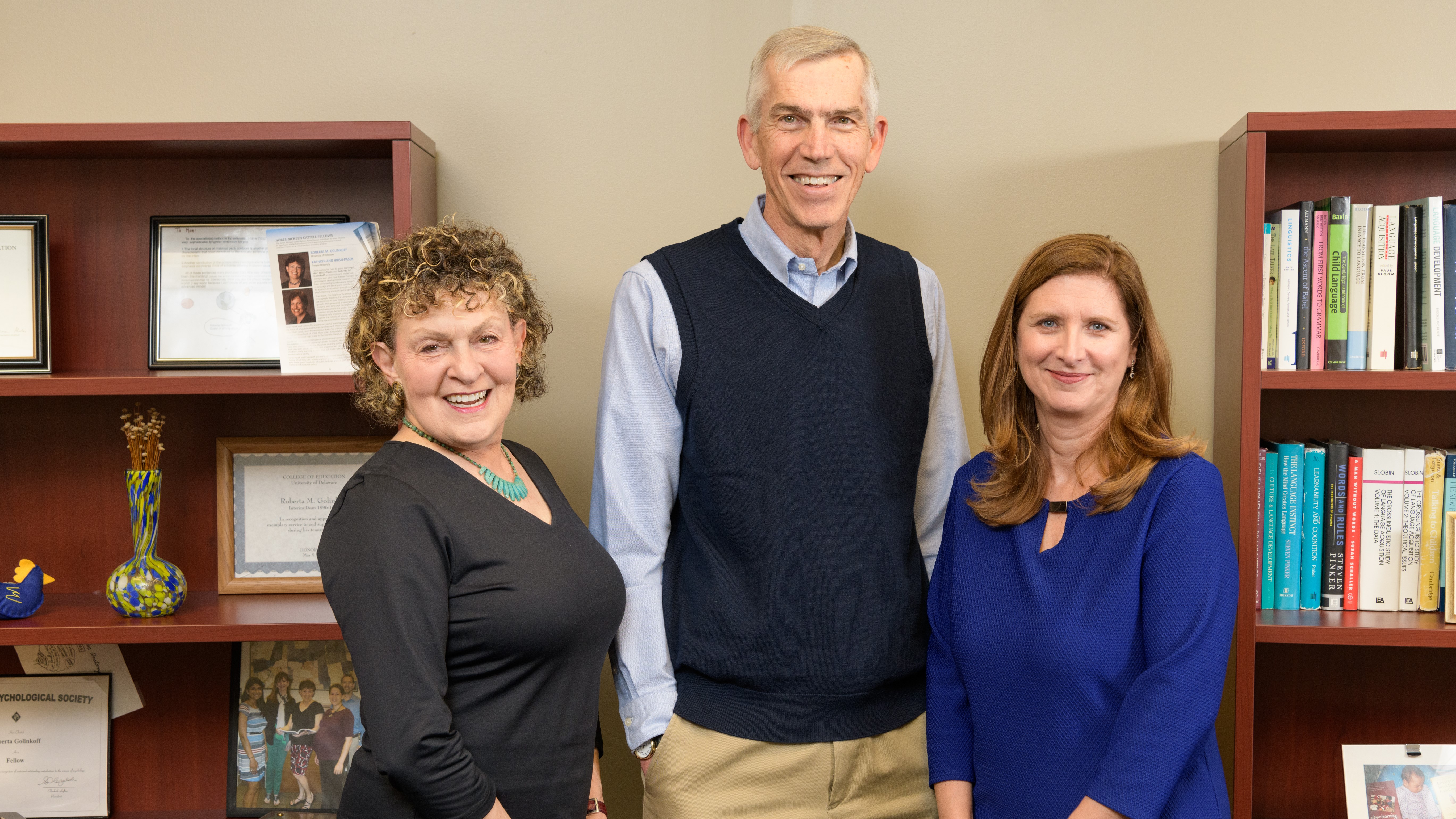 Three University of Delaware School of Education professors are 2019 AERA Fellows. From left to right: Roberta Golinkoff, James Hiebert, and Laura Desimone. They stand in front of bookshelves in one of their UD offices.