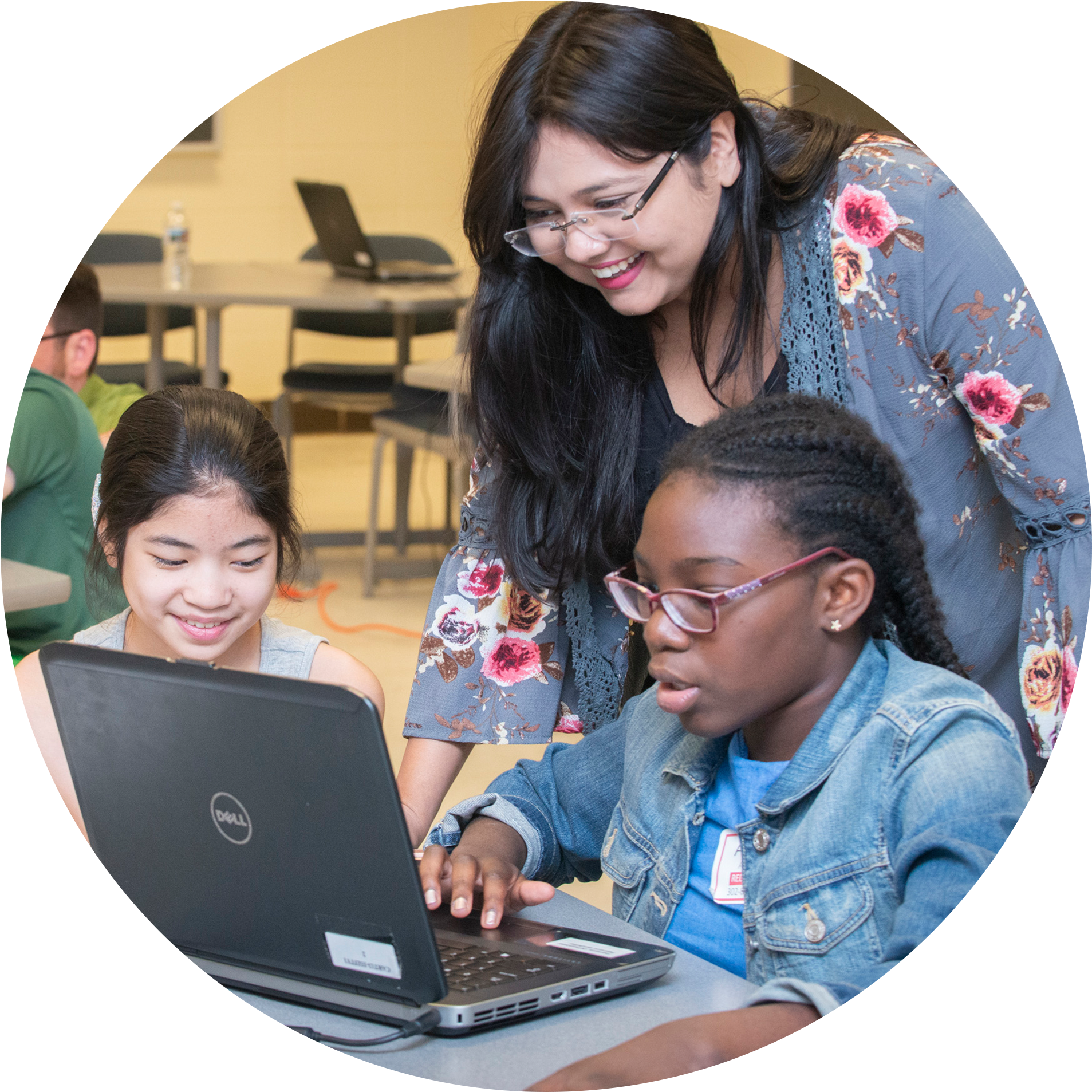 A teacher guides students on a laptop.