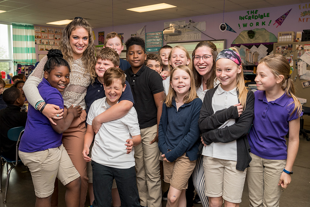 Two student teachers hug children in a classroom