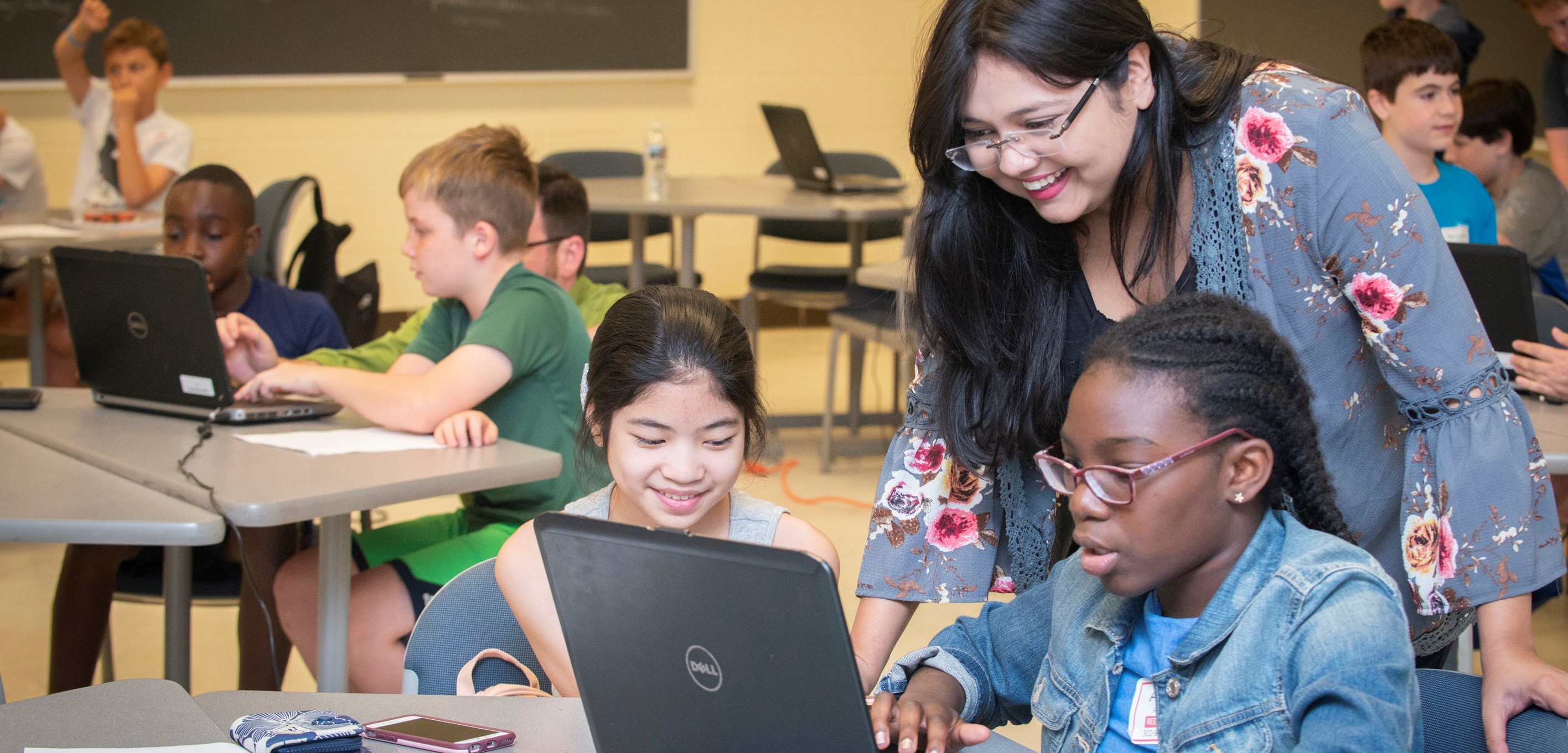 Teacher helps students at a table with a computer coding project.