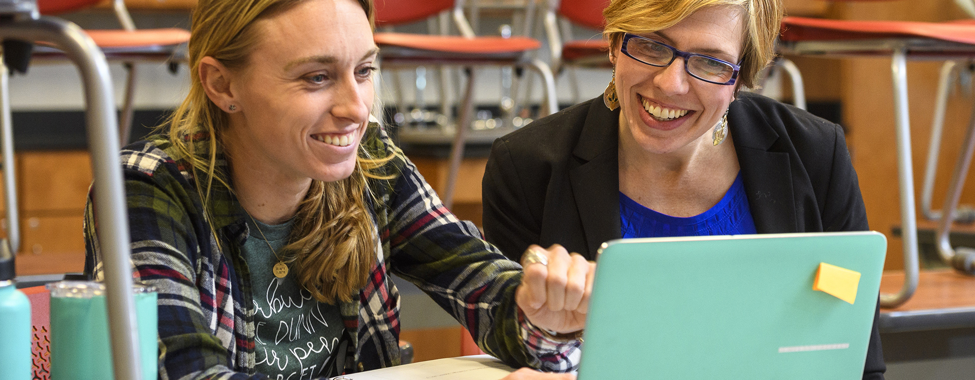 Professor and student review work on a laptop in a classroom.