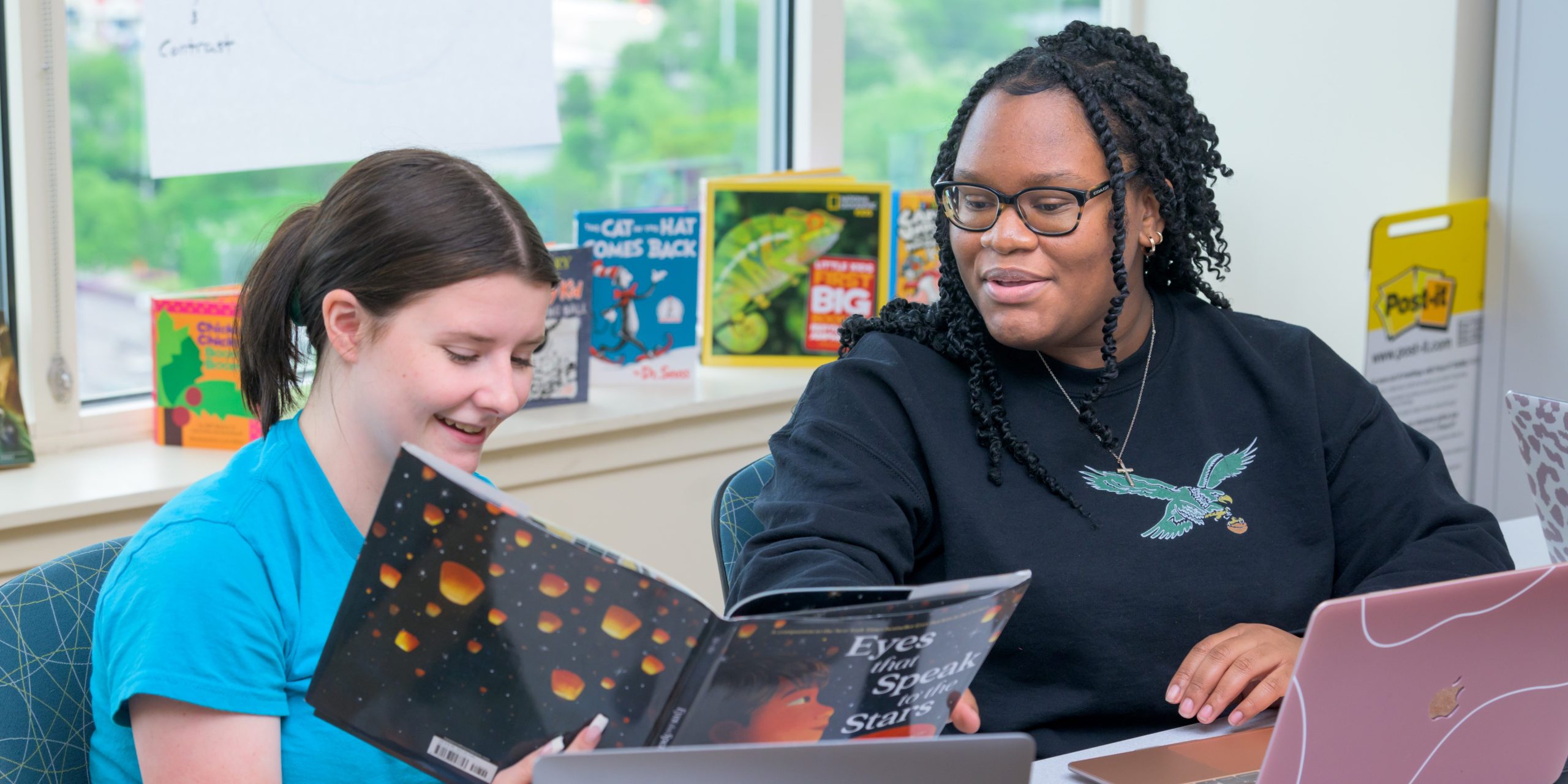 A student teacher reads to students in a classroom as they follow along in their books